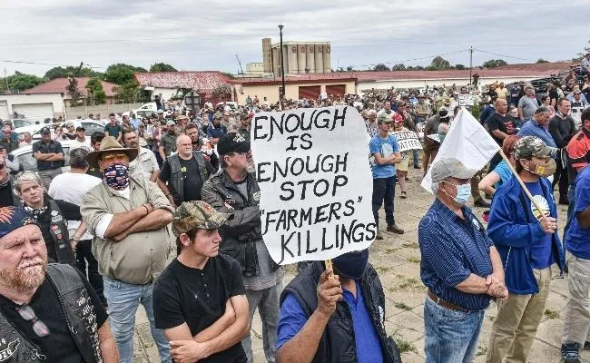 South African farmers and demonstrators gather at a protest against farm murders, holding placards demanding an end to killings.